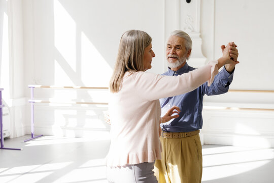 Bearded old man looking at his partner while dancing in ballroom