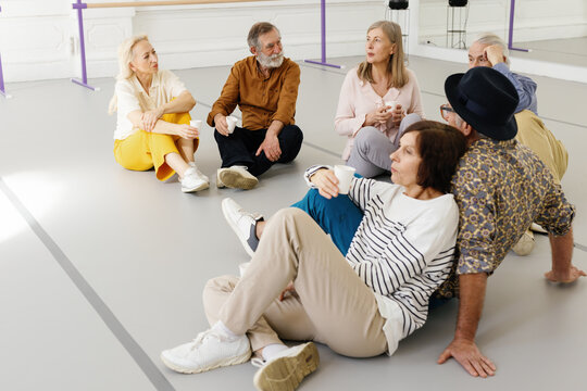 Elderly people drinking water while sitting on floor in ballroom 