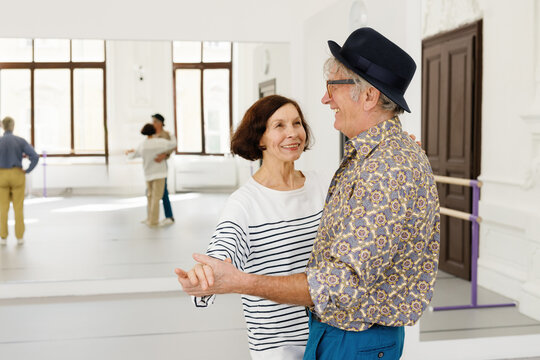 Pair of smiling retirees holding hands and dancing in ballroom