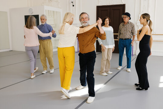 Retirees dancing in pairs under control of instructor at dance studio