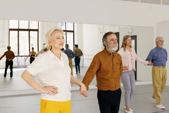 Pairs of retirees holding hands while dancing at dance studio