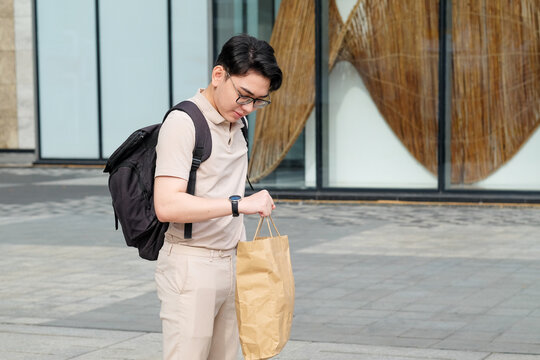 Man with shopping bag and backpack checking time on his watch