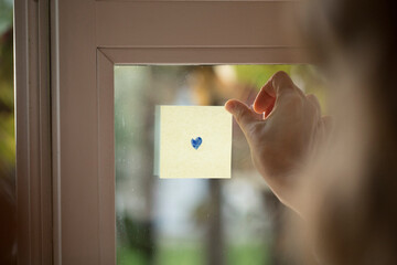 Hand Holding a Post-it with a drawn Heart on a Window