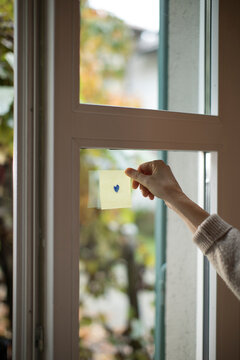Hand Holding a Sticky Note with a drawn Heart on a Window