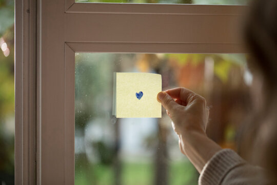Hand Holding a Sticky Note with a drawn Heart on a Window