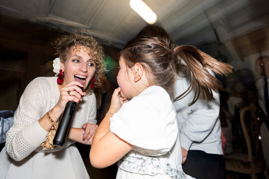 Woman singing with microphone and little girl dancing at party