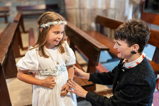 Woman adjusting girl's dress before her first communion in church