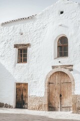 Fototapeta premium Historic whitewashed building with wooden doors and windows in a tranquil village setting showcasing traditional architecture