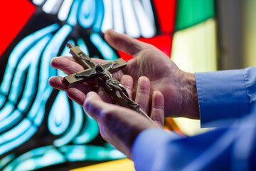 hands holding a cross in front of stained glass
