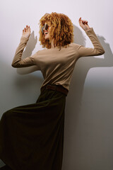 Stylish woman posing against a minimalist background, showcasing a trendy outfit with curly hair...