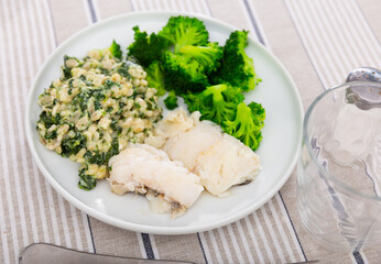 Cod with pearl barley porridge and boiled broccoli on a plate, side view. Low-calorie, nutritious lunch with fish and vegetables