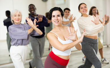 Positive sporty young Hispanic woman practicing modern vigorous dance movements in group dance class