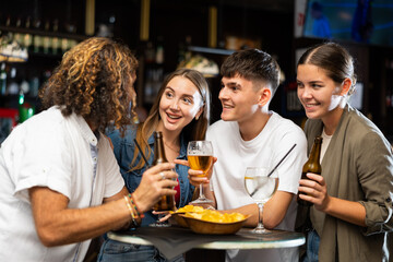 Two couples spending time in bar, having fun while drinking beer and talking.