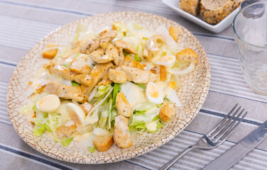 Caesar salad made from fresh iceberg lettuce, with chicken pieces and quail eggs on a ceramic plate. Serving a delicious salad on a round plate