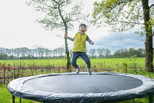 Child Joyfully Jumping on Trampoline in Green Outdoor Setting