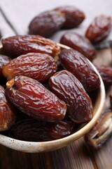 Many tasty dried dates in bowl on wooden table, closeup