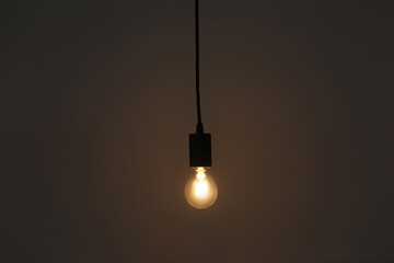 Glowing light bulb hanging on grey background