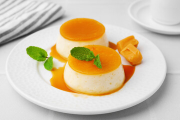 Tasty puddings with caramel sauce served on white tiled table, closeup