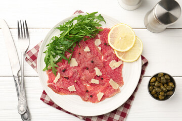 Fresh beef carpaccio with arugula, lemon and cheese served on white wooden table, flat lay