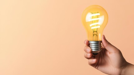A hand cradling a bright glowing lightbulb symbolizing creativity and ideas set against a soft pale orange background in a minimalistic style photo.