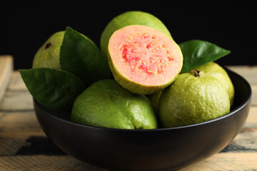 Fresh guava fruits in bowl on wooden table against black background, closeup