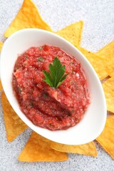 Spicy salsa sauce in gravy boat and nachos on light grey table, flat lay