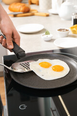 Man taking fried eggs from frying pan in kitchen, closeup