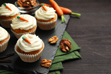 Tasty carrot muffins with cream, walnuts and fresh vegetables on black wooden table, closeup. Space for text
