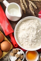 Rolling pin and ingredients for dough on wooden table, flat lay