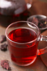 Delicious hibiscus tea in glass cup and dry roselle sepals on wooden table, closeup