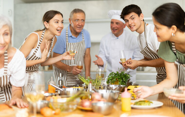 Cheerful learners of culinary classes engaged in spirited conversation around kitchen table while learning cooking fish