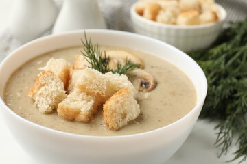 Delicious mushroom cream soup with croutons and dill served on white table, closeup