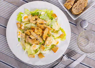 Caesar salad made from fresh iceberg lettuce, with chicken pieces and quail eggs on a ceramic plate. Serving a delicious salad on a round plate