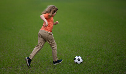 Obraz premium Kid playing football in the park. Child kicking a football ball on field. Happy boy running with a football ball. Children playing soccer outdoors. Kid play football on the grass. Summer soccer game.
