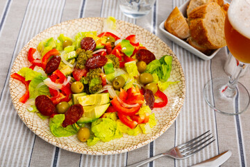 Fresh green salad with chopped avocado, roasted chorizo sausage, cherry tomatoes, pepper olives, pesto sauce and onion on plate