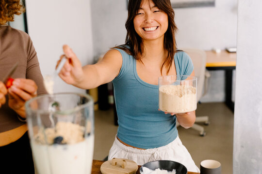 healthy woman pouring protein powder into a blender to prepare a shake
