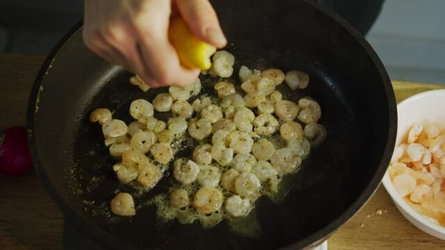 Shrimp fried in a hot pan in boiling oil are poured with lemon juice. The juice is squeezed out of the lemon to give the dish a tangy taste.