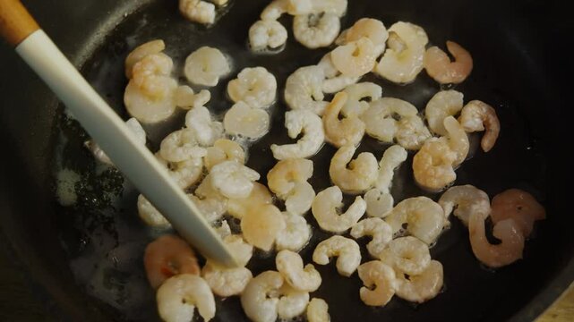 Fresh, thawed shrimp are fried in hot oil in a pan and flipped with a spatula to avoid burning.