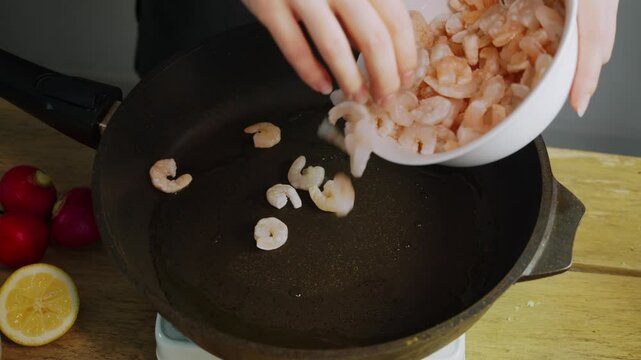 Chef lays out the frozen shrimp on a hot frying pan with oil and begins cooking them. The shrimp start to sizzle and smoke as they cook.