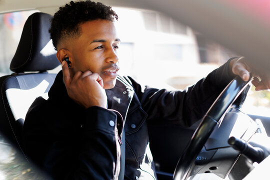 young driver man using earphones in the car in sunlight