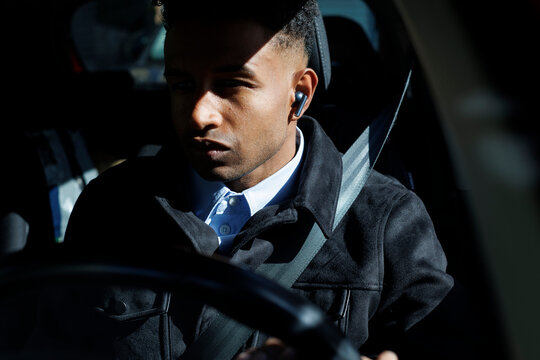 young driver using earphones in the car in sunlight in the city
