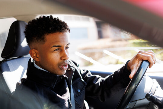 young driver using earphones in the car in sunlight in the city