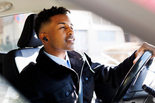 young driver using earphones in the car in sunlight in the city