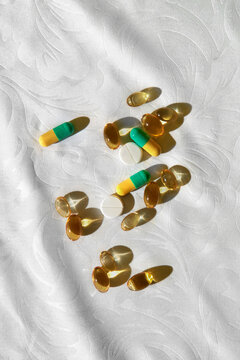 Many Omega 3 oil capsules and pills under sunlight on white tablecloth