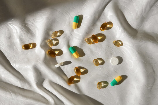 Many Omega 3 oil capsules and pills under sunlight on white tablecloth