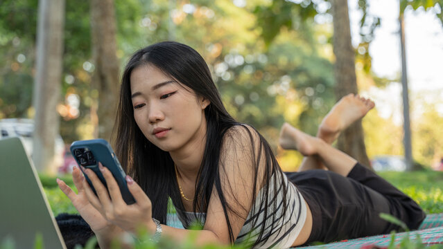 Beautiful young girl using mobile phone resting on the grass in a park - Powered by Adobe