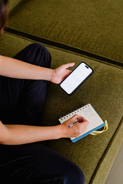 Unknown lady sitting in a couch handwriting notes and using a phone