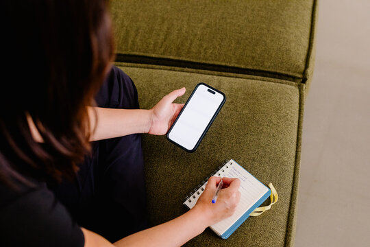 Anonymous woman using her smart phone while making handwritten notes