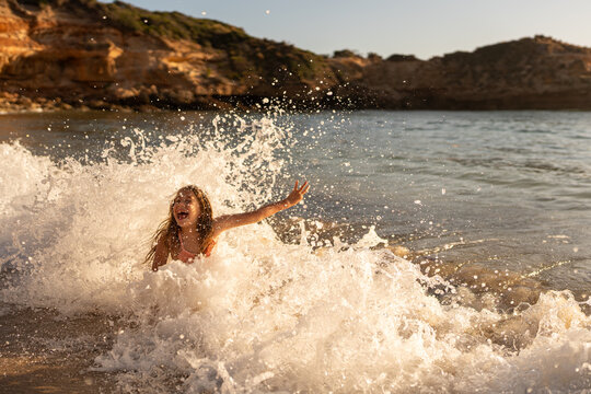 A young girl laughing as a wave splashes over her