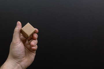 Hand holding a small brown cube against a black background. sembolyzing, cargo, delivery